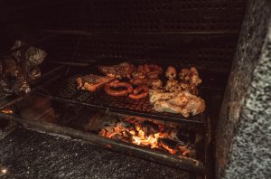 A barbeque pit with sausage links, chicken and steak over an open fire.